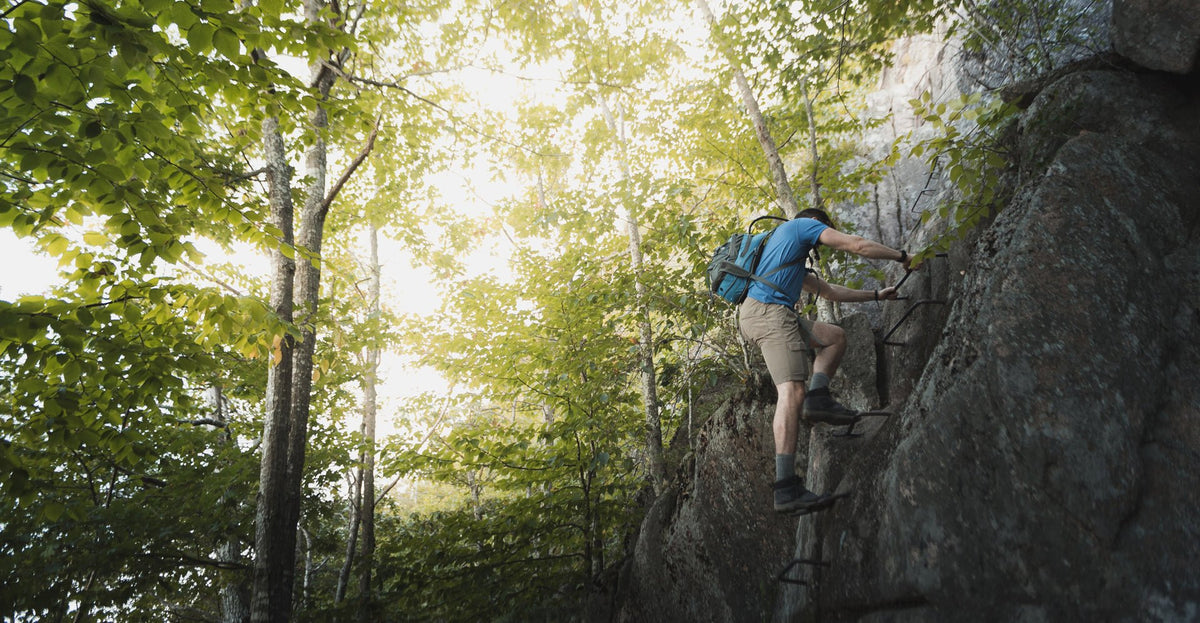 A hiker climbing iron rungs bolted into granite cliff on the Precipice Trail, Acadia National Park, Maine