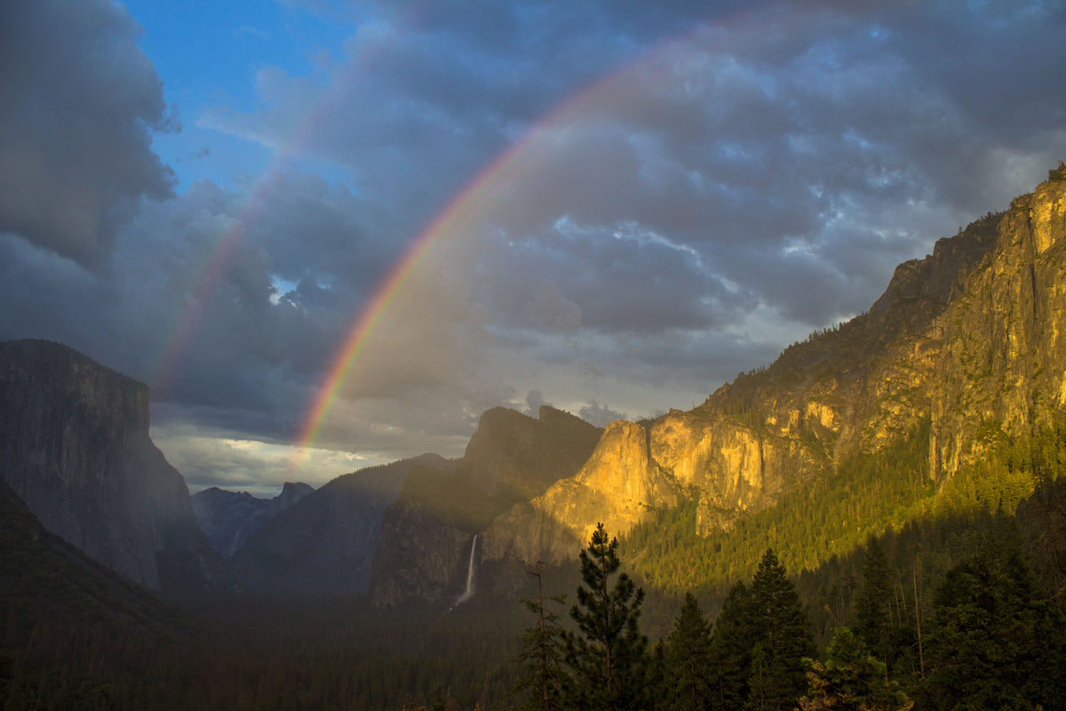 Rainbow and waterfall over Yosemite Valley with granite cliffs rising above the meadow floor. NPS photo