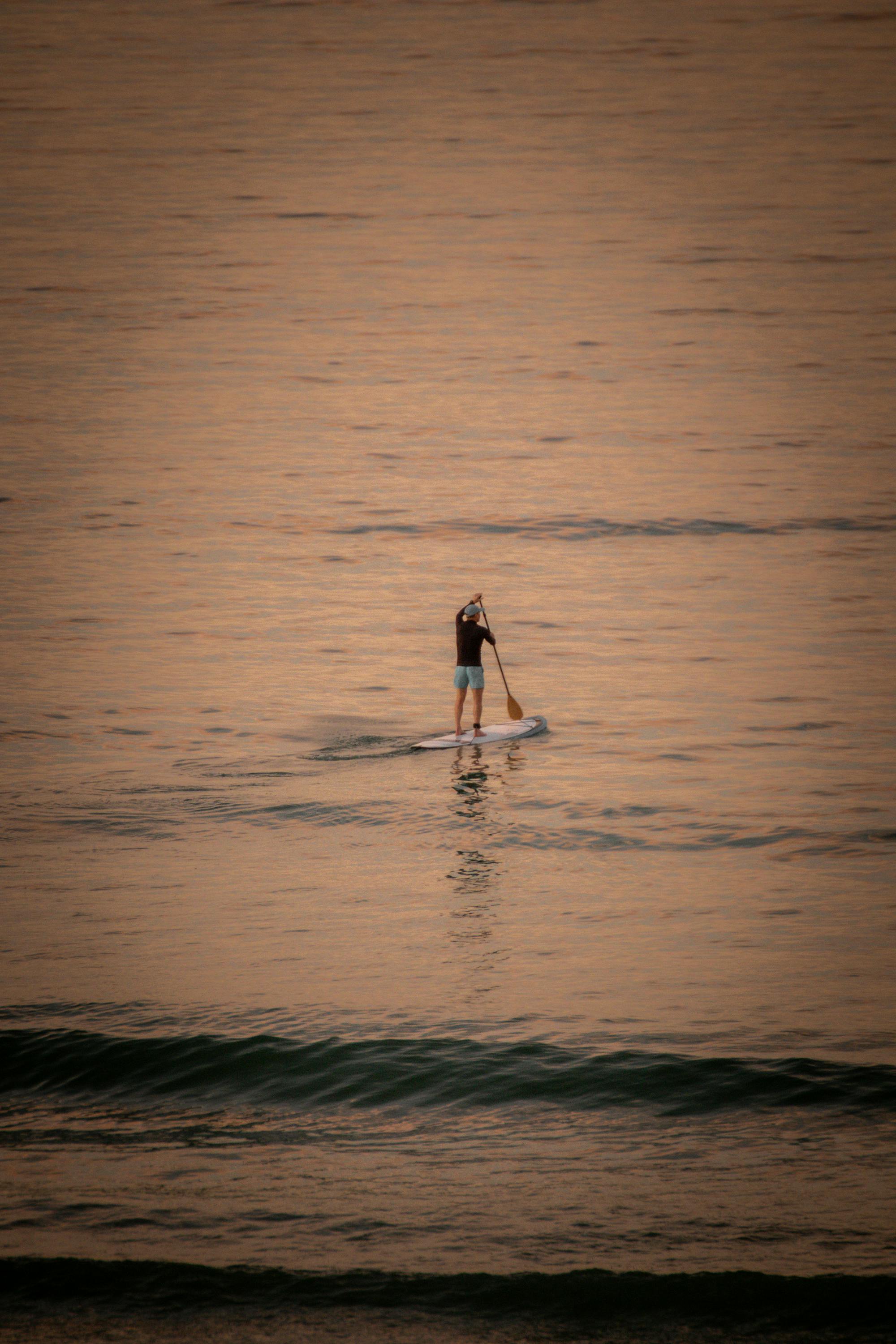 DOWNWIND — Lone paddleboarder on open ocean at golden sunset